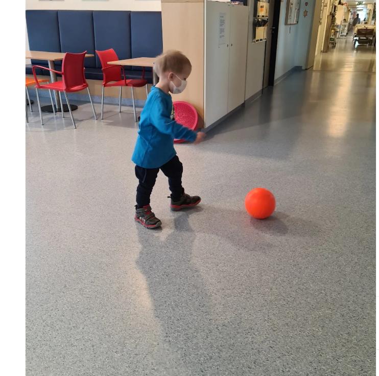 Thore läuft mit Maske und einem roten Ball über den Klinikflur.