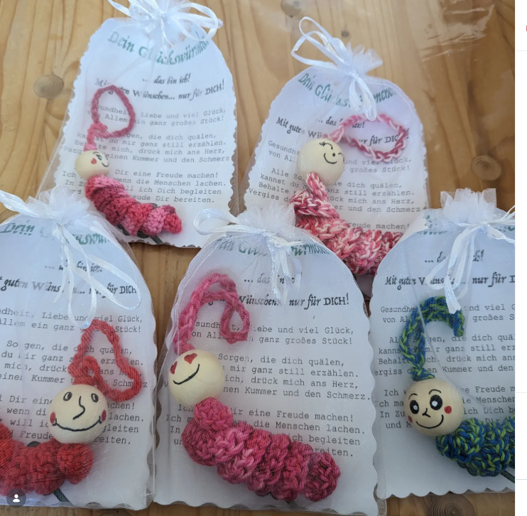 Mehrere gehäkelte Glückswürmchen liegen auf kleinen Geschenktüten mit Botschaften.