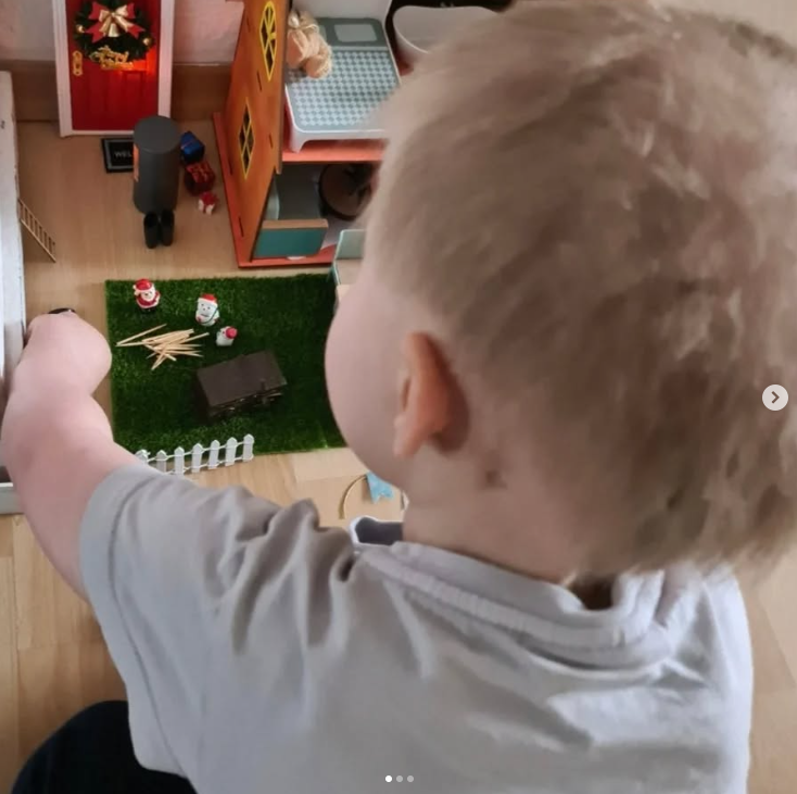 Ein Kind schaut in ein Puppenhaus mit kleiner Weihnachtsszene.